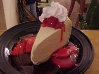 Slice of cheesecake topped with whip cream and strawberries